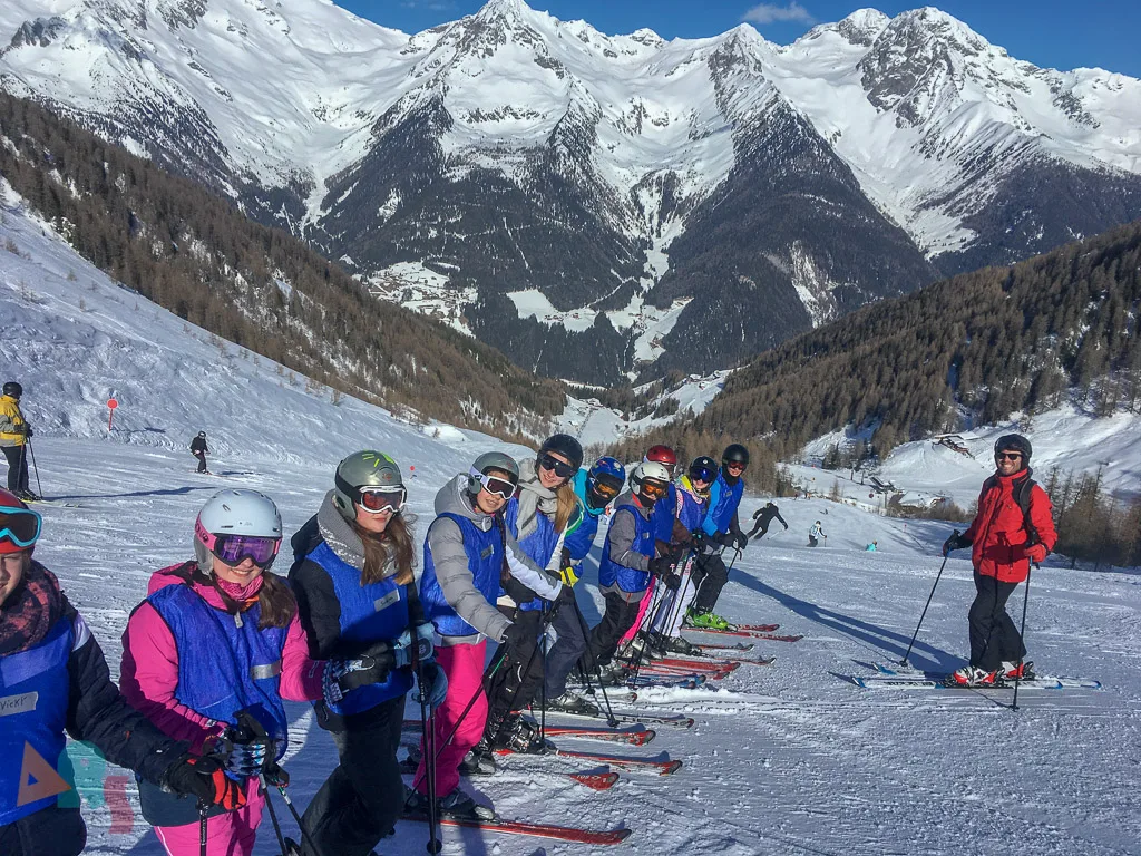 Skigruppe steht in einer Reihe vor den Gipfeln.